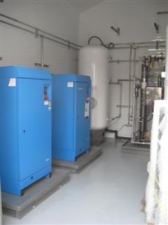 Blue compressor cabinets and a vertical air receiver in a plant room.